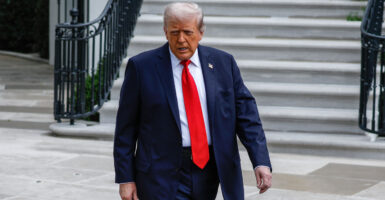 President Trump in a black suit and red tie walks in front of a staircase.
