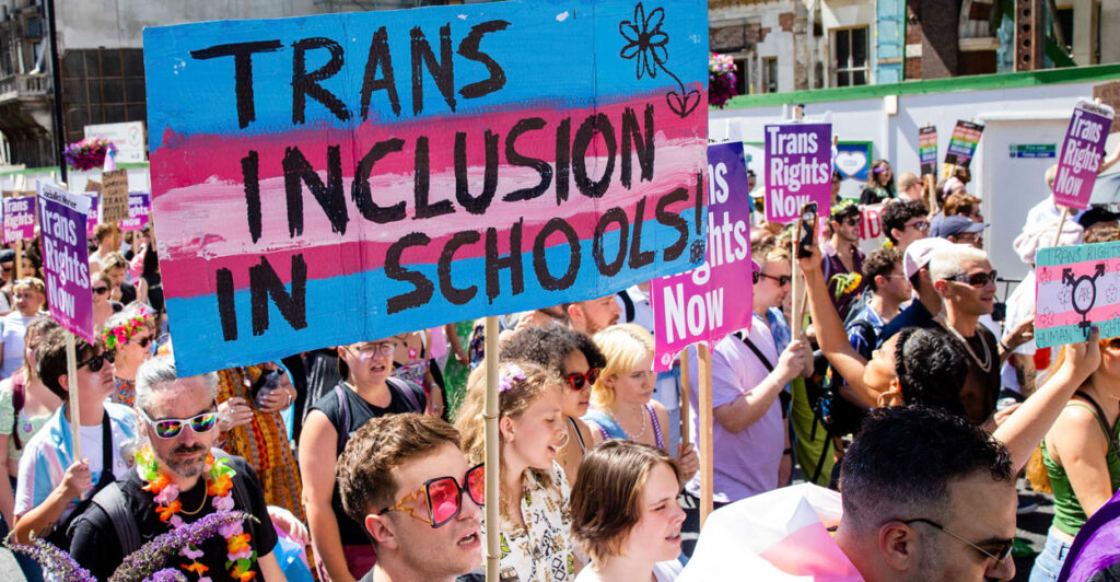 Protesters participate in a transgender pride rally, with one holding a sign that says trans inclusion in schools
