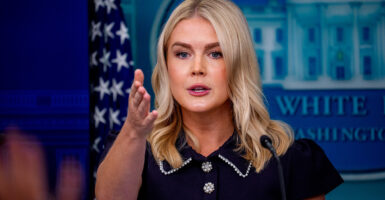 Karoline Leavitt in dark blue suit gestures with her right hand from White House podium.