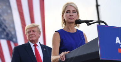 Rep. Mary Miller, R-Ill., speaks at a lectern with President Donald Trump looking on and with a U.S. flag as backdrop