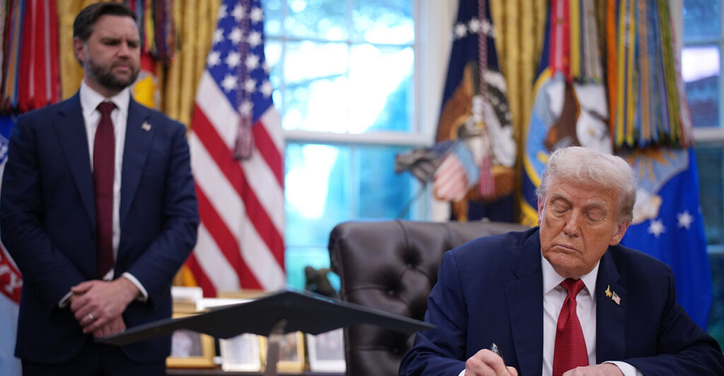President Trump signs an executive order in the Oval Office, with Vice President JD Vance standing over his right shoulder.