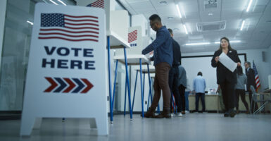 Vote here sign on the floor with people voting in booths at a polling station.