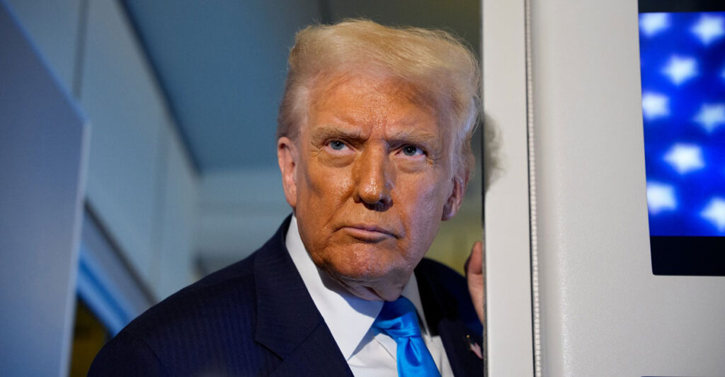 Donald Trump stands up with his head turned to his right as he listens to reporters asking him questions.