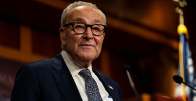 Chuck Schumer stands in front of a microphone and looks to his right.