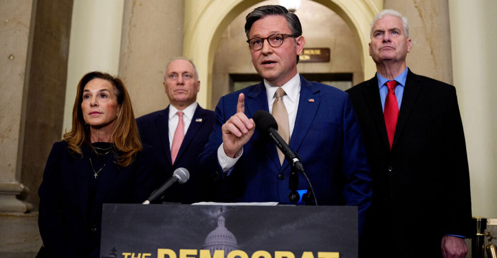 Mike Johnson stands at a podium and raises his right index finger as he speaks.