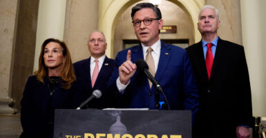 Mike Johnson stands at a podium and raises his right index finger as he speaks.