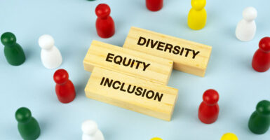 The words "diversity," "equity," and "inclusion" are written in all capital letters on three rectangular wood blocks, surrounded by red, yellow, green and white pegs.