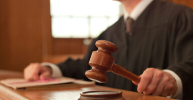 An unidentified judge in a black robe holds a gavel, poised to pound it.