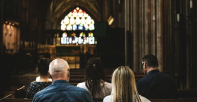 A view of a stained-glass behind the podium at a church, with parishioners in the pews, as seen from behind.