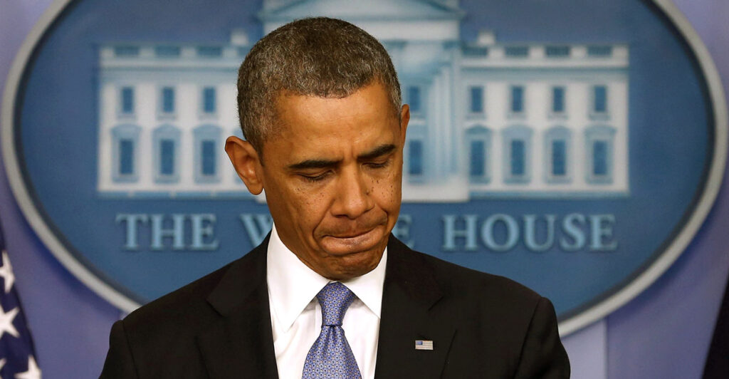 Barack Obama, with pursed lips and looking down, stands at White House press room podium.