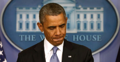 Barack Obama, with pursed lips and looking down, stands at White House press room podium.