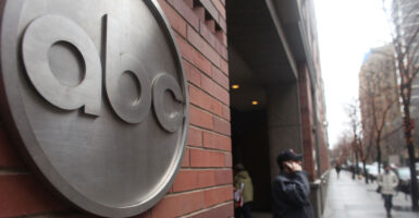 The ABC logo in silver on a brick building, as man stands with cellphone on sidewalk.