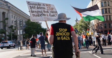 Man in black shirt with gold lettering reading "Stop Genocide in Gaza" and holding a sign walks down a Washington, DC street turning pro-Palestinian protest.