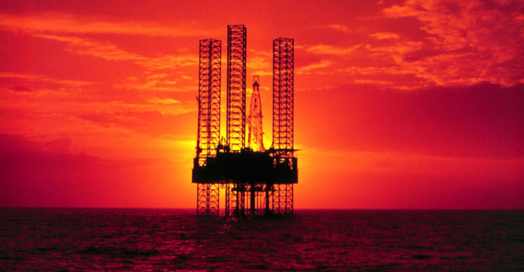 Silhouette of oil rig in Gulf of America against orange and red sunset.