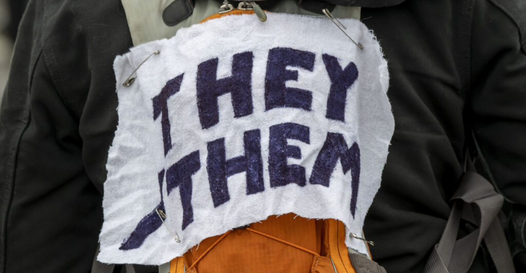 White arm band with black lettering, reading "They Them."