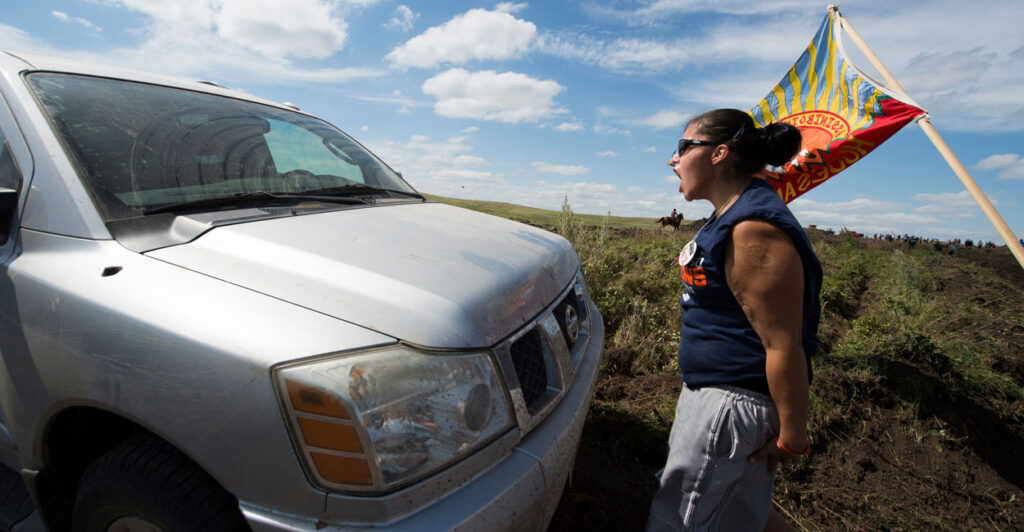 Protester in muscle shirt and shorts stands in front of a white truck screaming during 2016 protest.