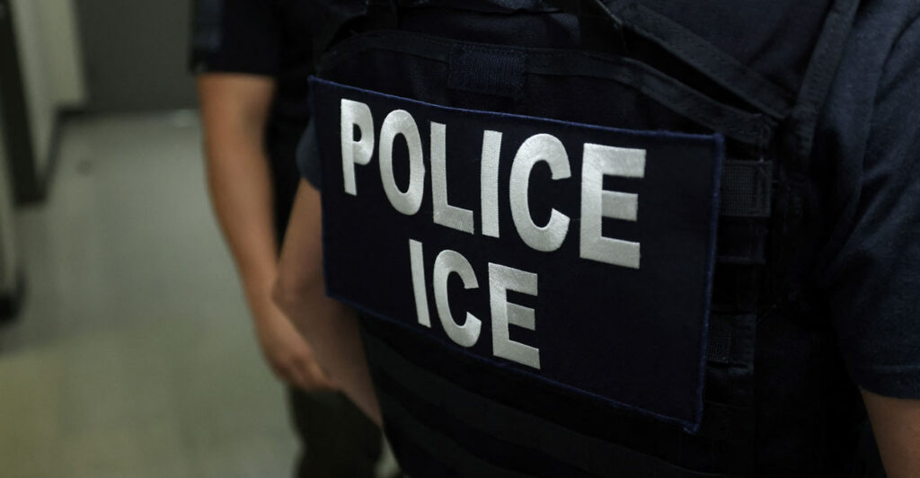 Back of an ICE agent in black uniform reading "Police ICE" in white lettering.
