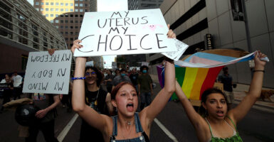 A female pro-abortion protester holds a sign reading "my uterus my choice" next to a woman holding an LGBTQ flag.