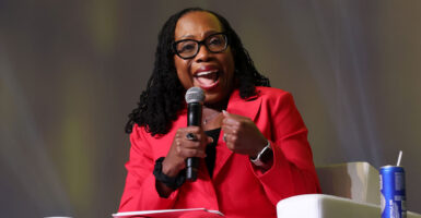 Justice Ketanji Brown Jackson in a red jacket and pants sitting in a white chair, speaks.