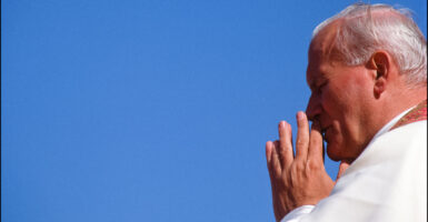 Close-up profile of Pope John Paul II praying against a perfect blue sky.