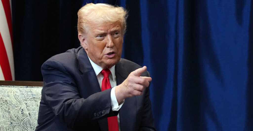 Donald Trump, seated, points.