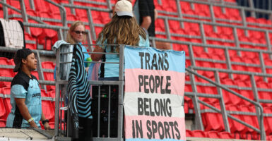 A sign hanging on the railing of a stadium reads "TRANS PEOPLE BELONG IN SPORTS"