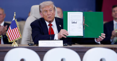President Trump holds up the signed Gaza peace agreement, while sitting down.