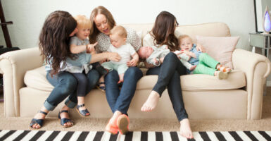 Three mothers sit with four little children on a couch.