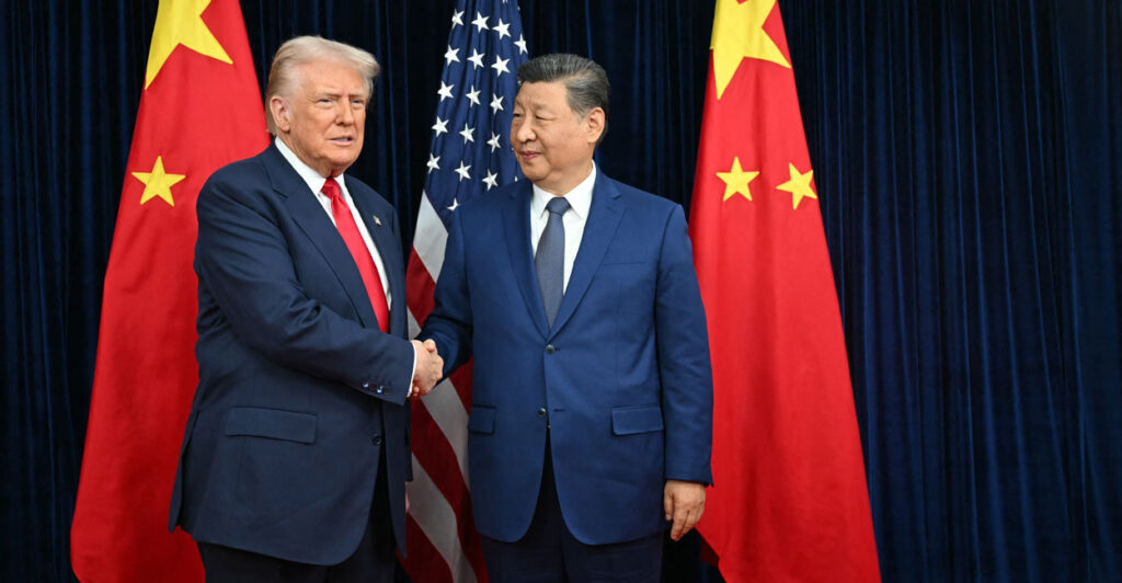 President Donald Trump and Chinese leader Xi Jinping shake hands in front of Chinese and American flags.