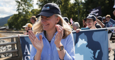 Abigail Spanberger smiling and clapping as she walks in front of supporters wearing a hat.