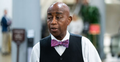 Chaplain of the Senate Barry Black walks through the Capitol wearing a white shirt, black vest, and bowtie.