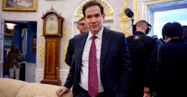 Secretary of State Marco Rubio is standing near a sofa, looking directly at the camera.