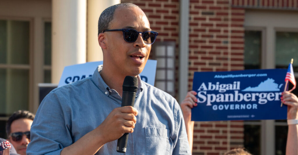Democrat Virginia attorney general candidate Jay Jones in a blue button-down shirt with sunglasses on holding a microphone and speaking outdoors to supporters