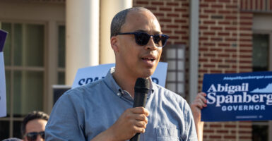 Jay Jones in blue shirt and wearing sunglasses speaking with a microphone.
