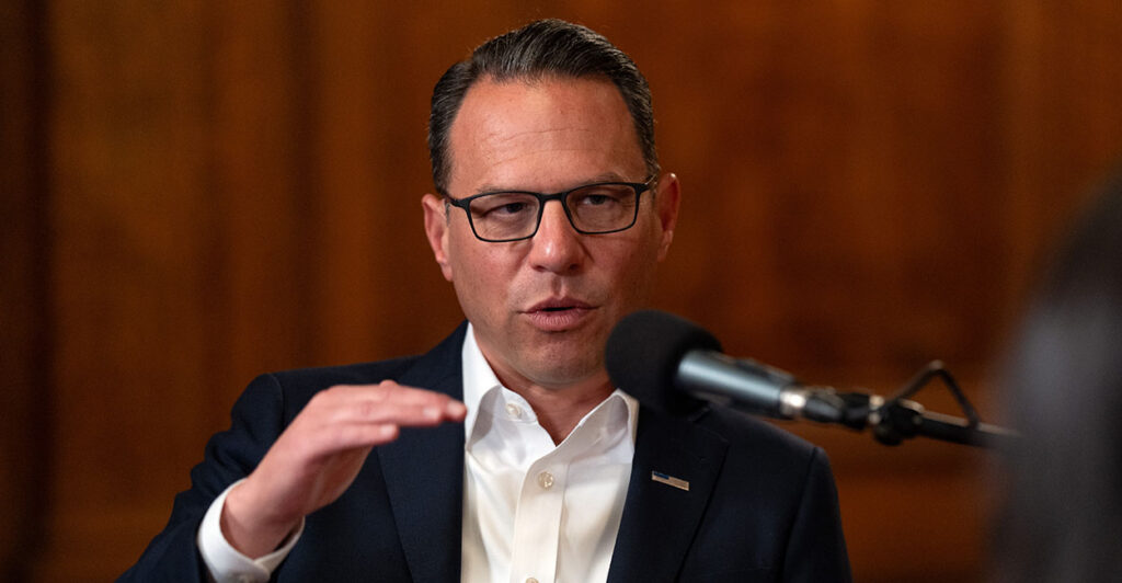 Josh Shapiro in a suit gestures in front of a microphone. Shapiro has condemned Jay Jones' tweets but hasn't called for him to drop out of the race
