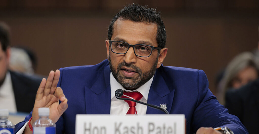 FBI Director Kash Patel, in a blue suit, makes the "OK" sign