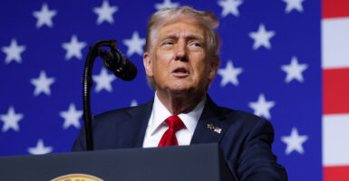 Donald Trump in a blue suit with a red tie in front of an American flag