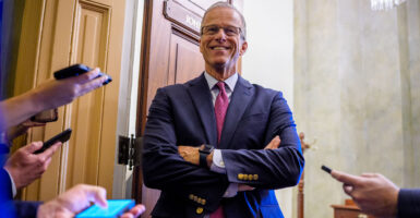 Senate Leader John Thune smiles in front of his office while talking to reporters.