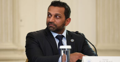 Kash Patel, seated, with a glass of water in front of him, looks to his right.