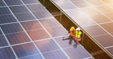 Aerial view of two solar energy technicians examining large solar panels in a field.