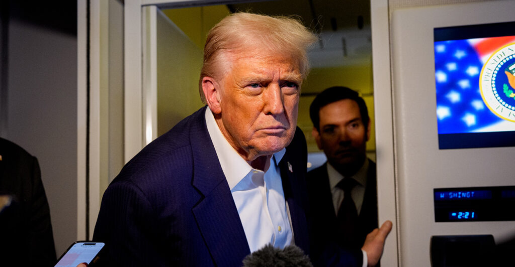Trump, in blue jacket and open-collar white shirt stares at a reporter aboard Air Force One.