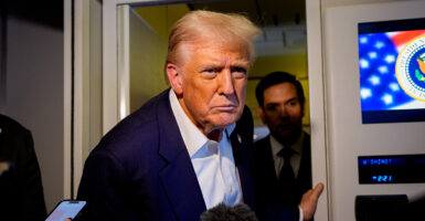 Trump, in blue jacket and open-collar white shirt stares at a reporter aboard Air Force One.
