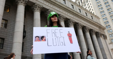 A young woman stands in front of a courthouse holding a sign reading "Free Luigi."