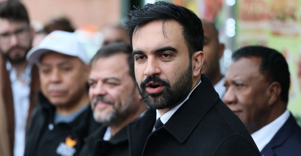 Zohran Mamdani stands outside during a press conference and looks to his left.