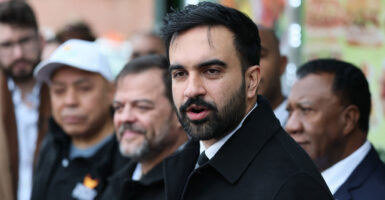 Zohran Mamdani stands outside during a press conference and looks to his left.