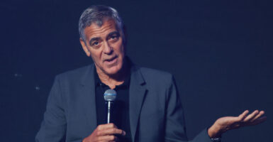 Actor George Clooney, with a microphone in his right hand and gesturing with his left hand