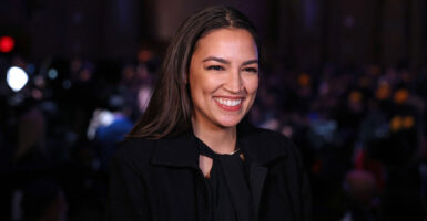 Alexandria Ocasio-Cortez stands at an event and smiles while she celebrates.