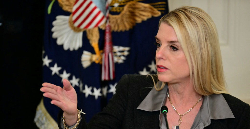 Pam Bondi sits before a microphone and gestures with her right hand.