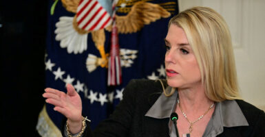Pam Bondi sits before a microphone and gestures with her right hand.