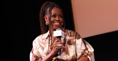 Michelle Obama sits in a chair and holds a microphone in her right hand as she turns to the left.